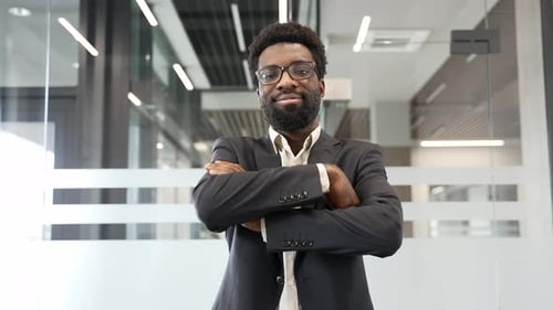 Portrait of African American businessman confidently smiling with crossed arms in a modern office.