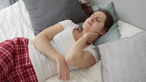 Woman Massaging Stiff Neck While Lying in Bed