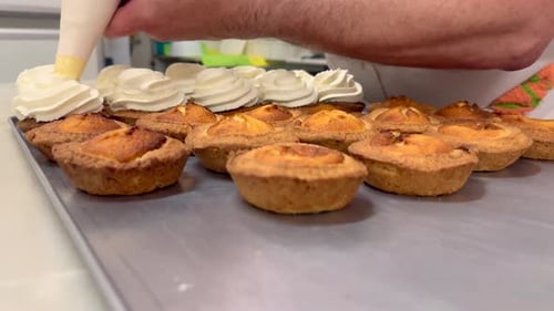 Un pâtissier ajoute de la crème à des gâteaux récemment préparés avec une poche à douille sur un plateau en métal