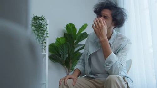 Asian young upset depressed man sitting alone in living room at home.