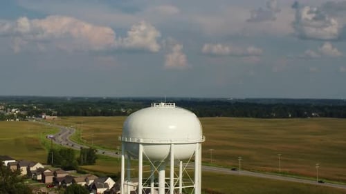 Water Tower With Vehicles Driving Through Fields On A Sunny Day. - aerial dolly, zoom out