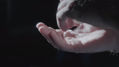 Männliche Hand gießt weiße runde Pillen in die Handfläche auf schwarzem Studiohintergrund