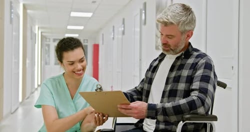 Nurse Assisting WheelchairBound Patient in Hospital Corridor