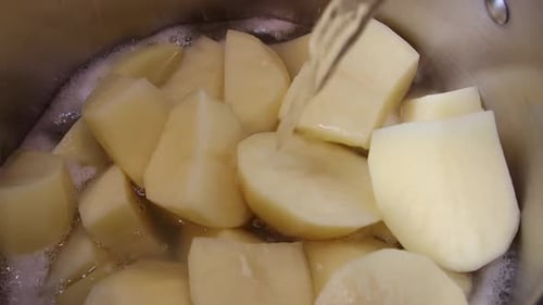 Água fervente sendo derramada sobre batatas fatiadas cozinhando em uma panela. Diminua o zoom.
