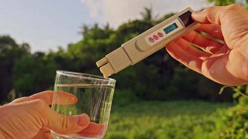 Vue à la première personne des mains mesurant la pureté de l'eau potable avec un testeur numérique montrant vingt ppm