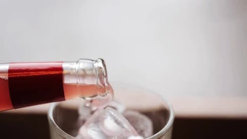 Refreshing pink beverage pouring over ice cubes