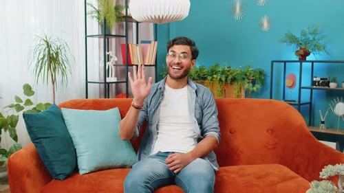 Man Smiling and Waving Hello on Couch Indoors
