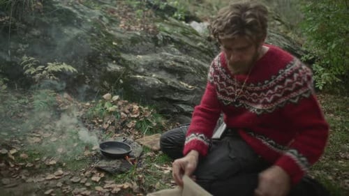 Man Preparing to Cook Meat over Campfire during Survival Trip in Forest