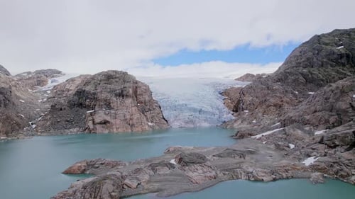 Drone Flying Towards Norwegian Glacier Through Rocky Landscape And Fjord