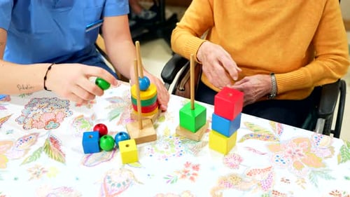 Nurse Assisting Elderly Woman Playing with Building Blocks