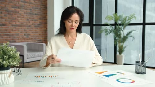 Businesswoman Reviews Data Charts in a Modern Office