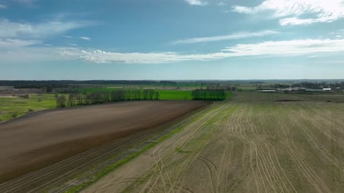 Aerial view of a brown and green field with a road dividing the two. The brown fields have distinct