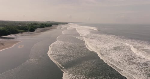 Aerial dolly over vast stretch of black sand beach with waves running in