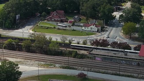 Aerial top down shot showing departing train leaving train station beside road with driving cars in