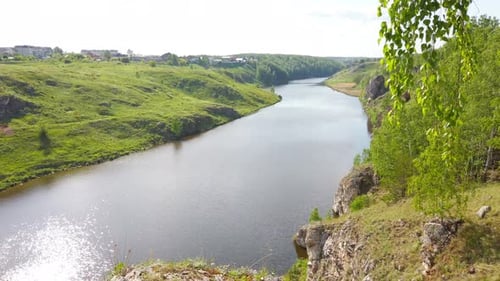 Grünes Baldachin über dem Fluss, sonniger Blick auf die Hängebrücke am felsigen Ufer