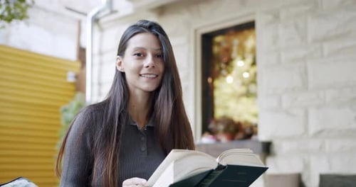 Young Brunette Reading Book on Street