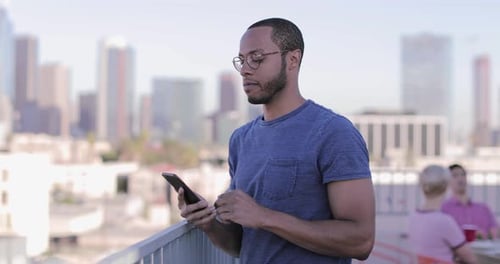 Man Using Smartphone on Rooftop with City View