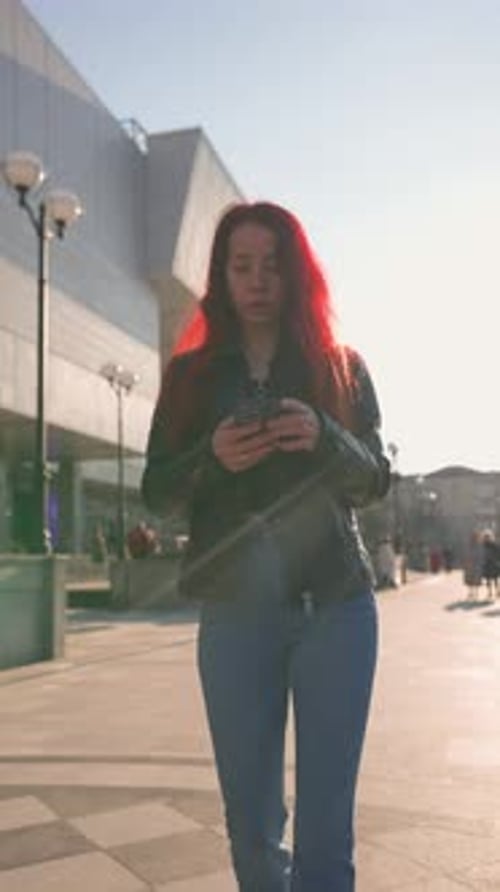 Serious Woman with Slim Figure Walks on City Park and Texts Using Smartphone