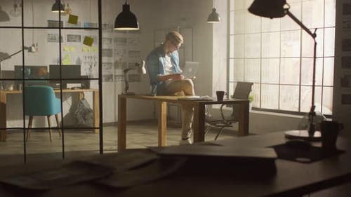 Professional Creative Designer Holds Laptop, Walks around His Office Checking Product Drawings and