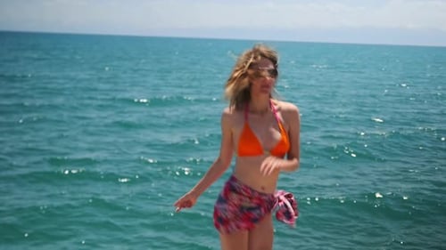 Attractive slender young woman dancing on the beach, enjoying summer vacation in a seashore