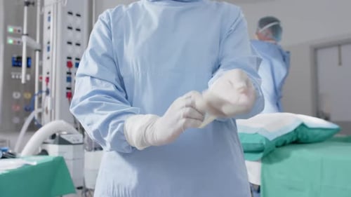 Medical Professional Puts on Surgical Gloves in Operating Room