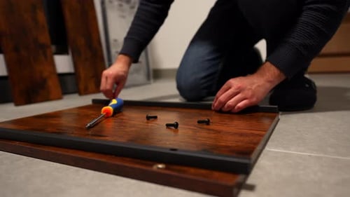 Close-up of male hands assembling wooden furniture with screwdriver on floor