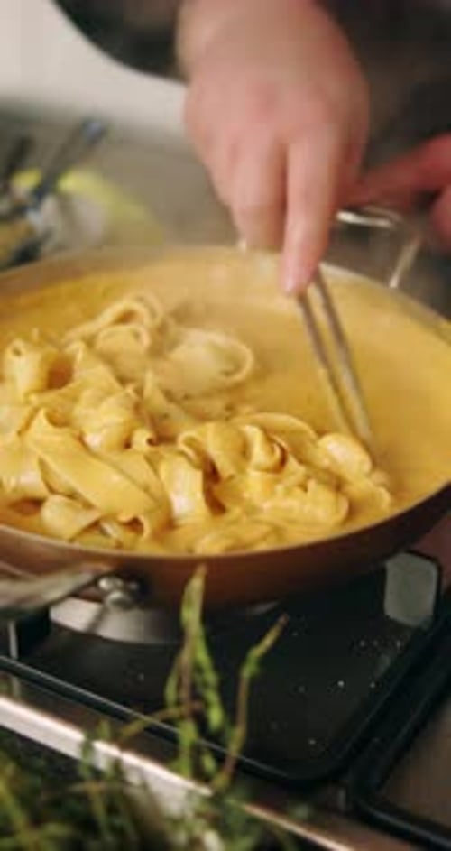 Person stirs pasta in creamy sauce on stove