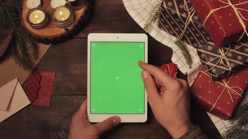 Top View of Hands Scrolling and Taping On Vertical Green Screen of Brand New White Tablet on Wooden