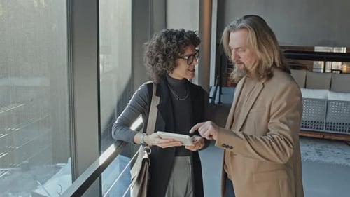 Man and Woman with Tablet Talking in Office Lobby while Waiting for Taxi