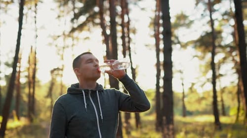 a Man in the Forest or in the Park Drinks Water From a Plastic Waste Bottle After a Hard Jogging
