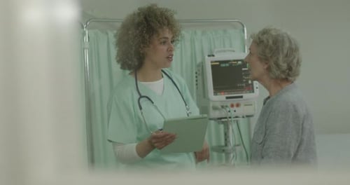 Female Nurse Examining Senior Patient in Hospital, taking notes on Digital Tablet
