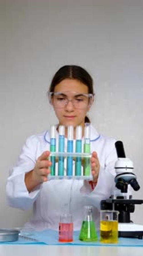 Girl Holding Colorful Test Tubes Next to Microscope