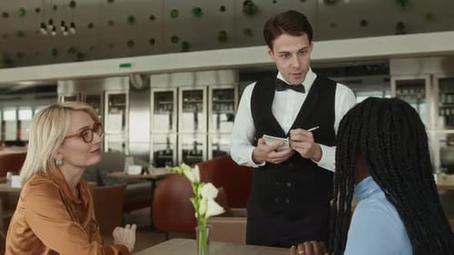 Young Waiter Taking Orders from Diverse Female Guests in Fancy Restaurant