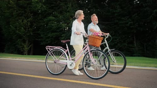 Senior Family of Two Having Promenade with Bicycles Outdoors