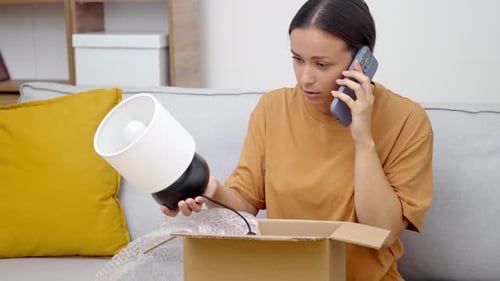Woman on Phone Unpacking New Lamp From Box