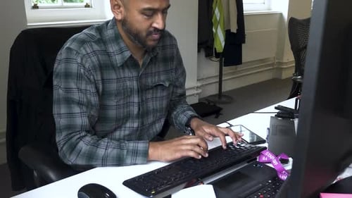 Close up shot of a man typing on his desktop pc on computer table in office at daytime.