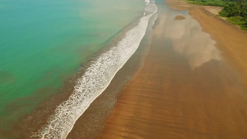 Aerial view of turquoise Pacific Ocean waves meeting sandy shore in Costa Rica