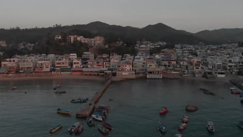 An aerial revealing view of an oceanfront town located in a bay surrounded by trees and nature.