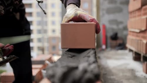 Trabalhador colocando tijolo sobre argamassa no canteiro de obras