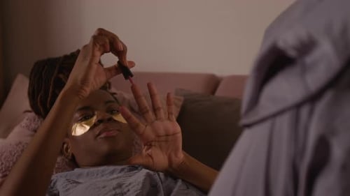 African American Girl Lying on Bed, Painting Nails at Cozy Pajama Party