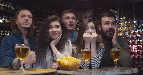 Young Football Male and Female Fans Watching Game Together in Evening in Pub and Cheering Up for