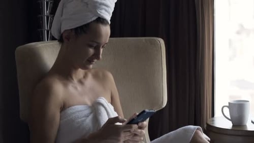 Woman in Towel Relaxing, Using Smartphone in Hotel Room