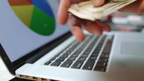 Laptop showing data and money stack close up