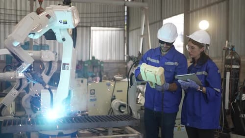 Blue collar workers at machine shop with welding robot arm.
