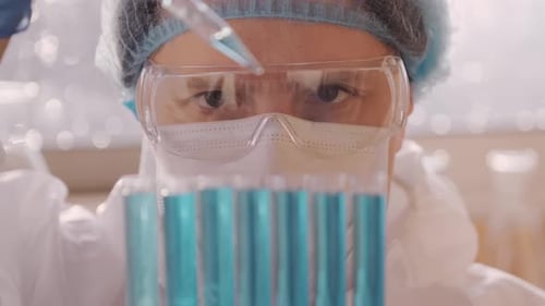 Scientist Man Wearing Goggles and Gloves Dripping Blue Liquid Into Test Tube with Pipette in