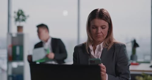 Businesswoman using smartphone in office, colleagues in background