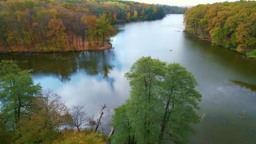 Curved banks of the narrow river overgrown with trees. Beautiful colors of nature on autumn season.