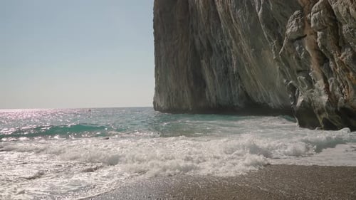 Majestic Cliff Overlooks the Shimmering Sea as Waves Gently Crash onto the Rocky Shoreline, Bathed