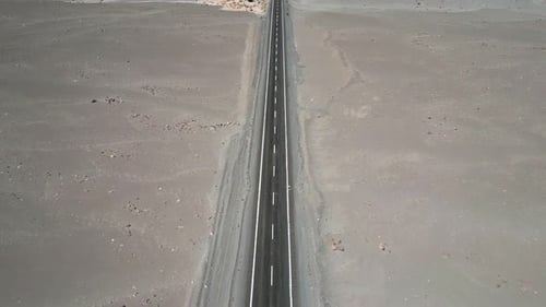 Forward ascending reveal along endless straight paved highway cutting through pale arid desert
