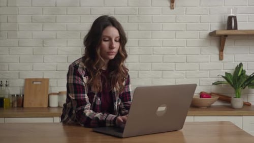 Woman working on laptop in bright kitchen
